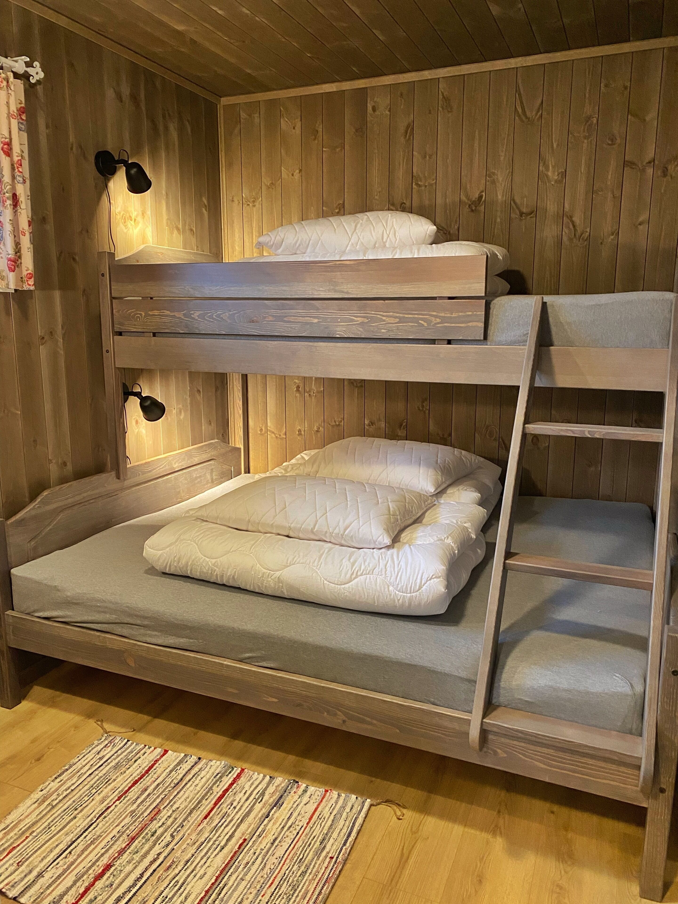 A bunk bed with two levels, a wooden floor, a striped rug, and a curtain with floral patterns.