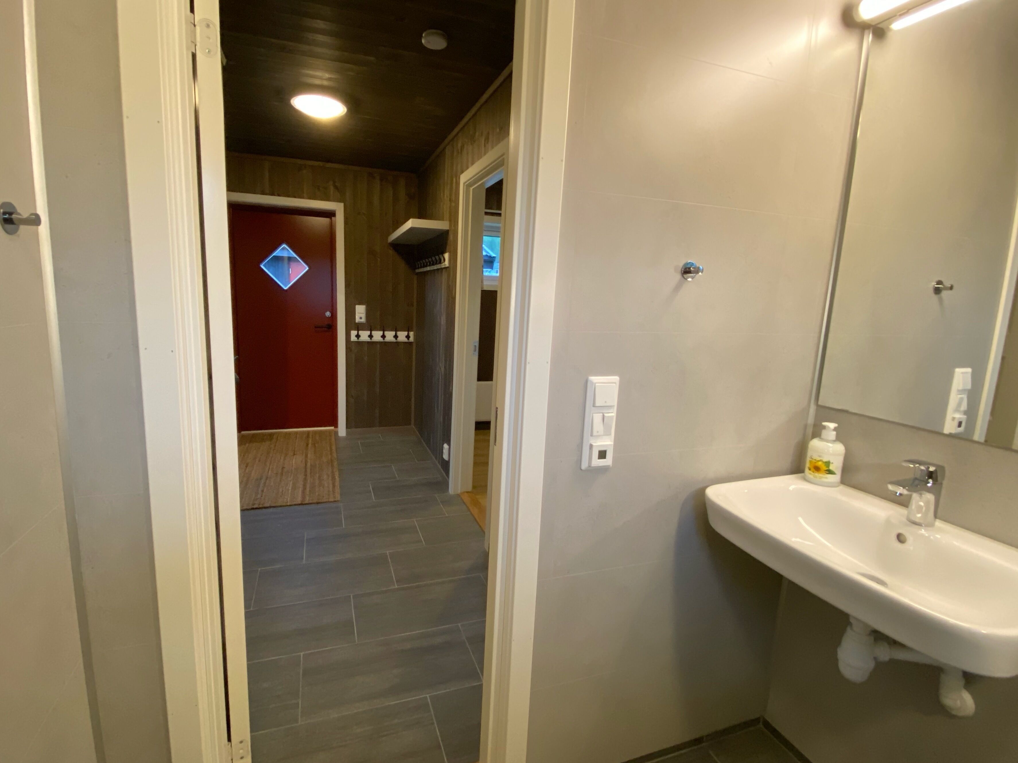 Un baño con un lavamanos blanco, un espejo y una puerta roja al fondo.