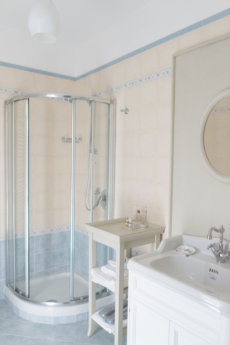 A bathroom with a glass-enclosed shower, a sink with a mirror, and a small table with toiletries.