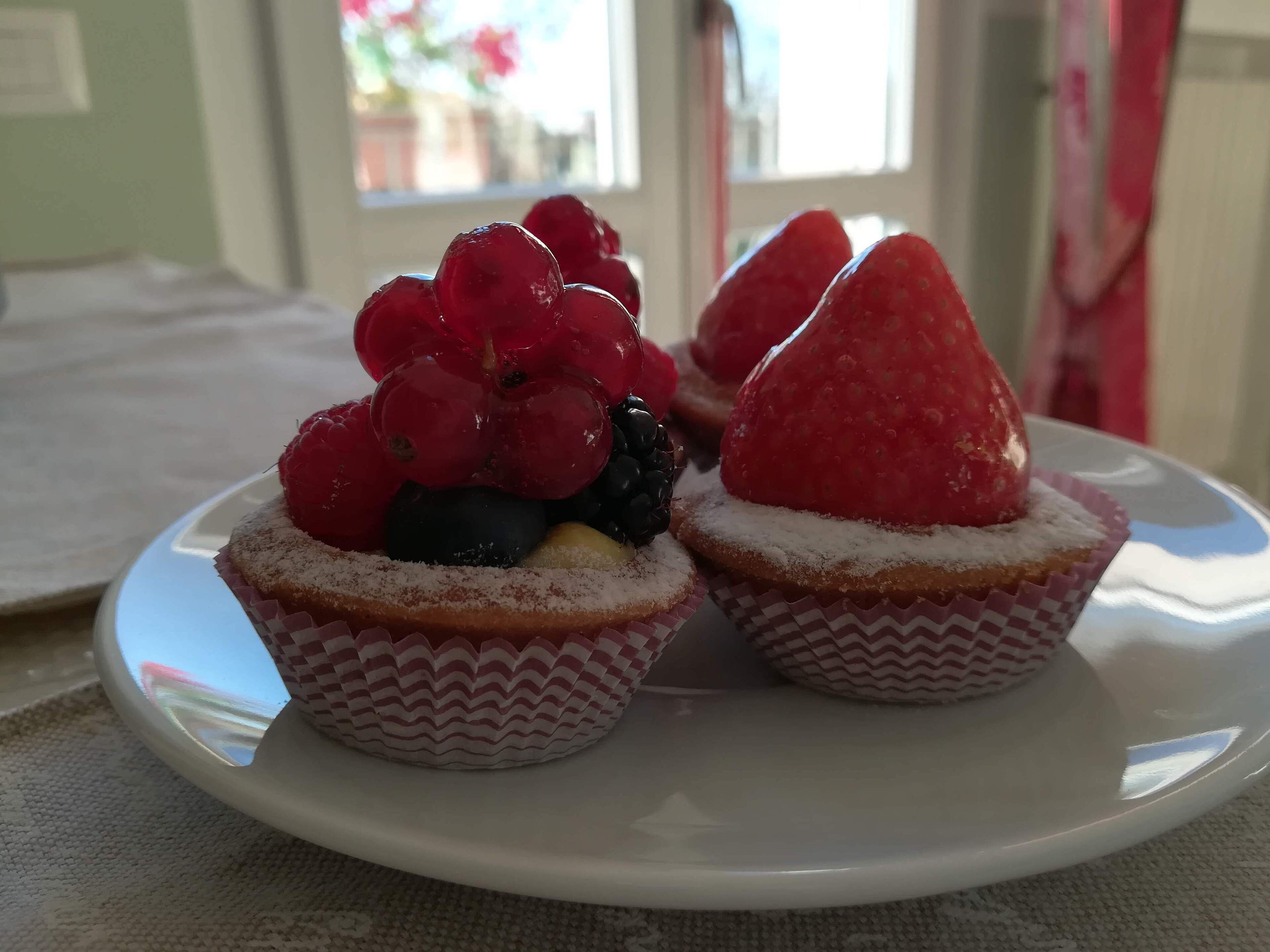 Two cupcakes with fruit toppings on a white plate.