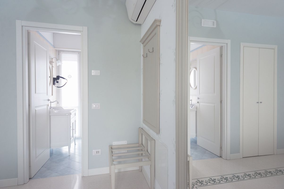 A hallway with white doors, a small bench, and a light switch on the wall.