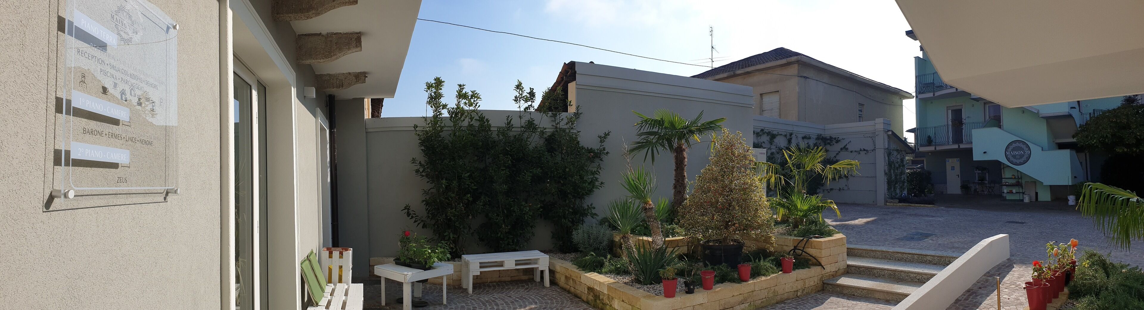 A courtyard with a white bench, potted plants, and a sign listing amenities like a piano and reception.
