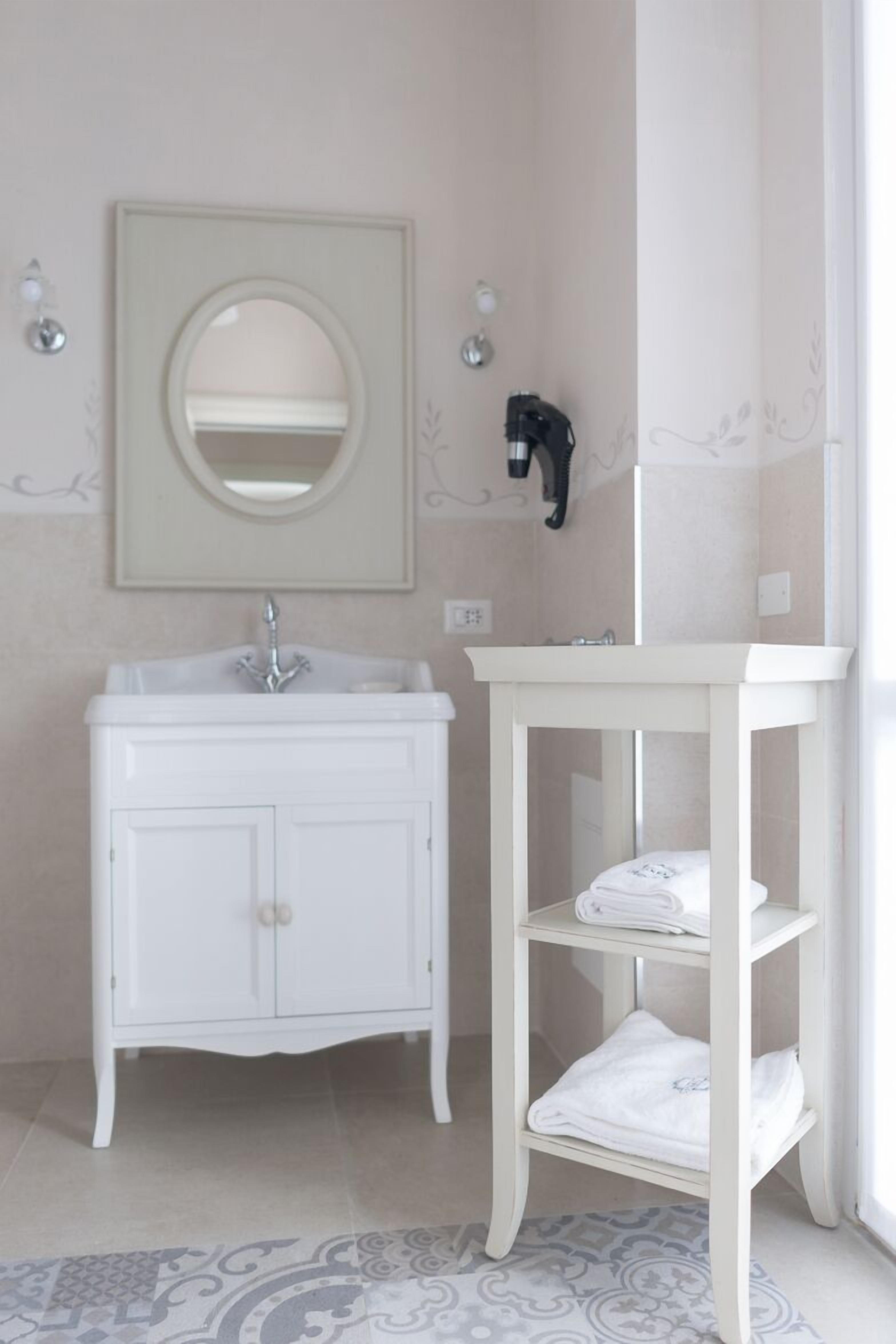 Een badkamer met een wit wastafelmeubel, een ronde spiegel en een witte plank met handdoeken.