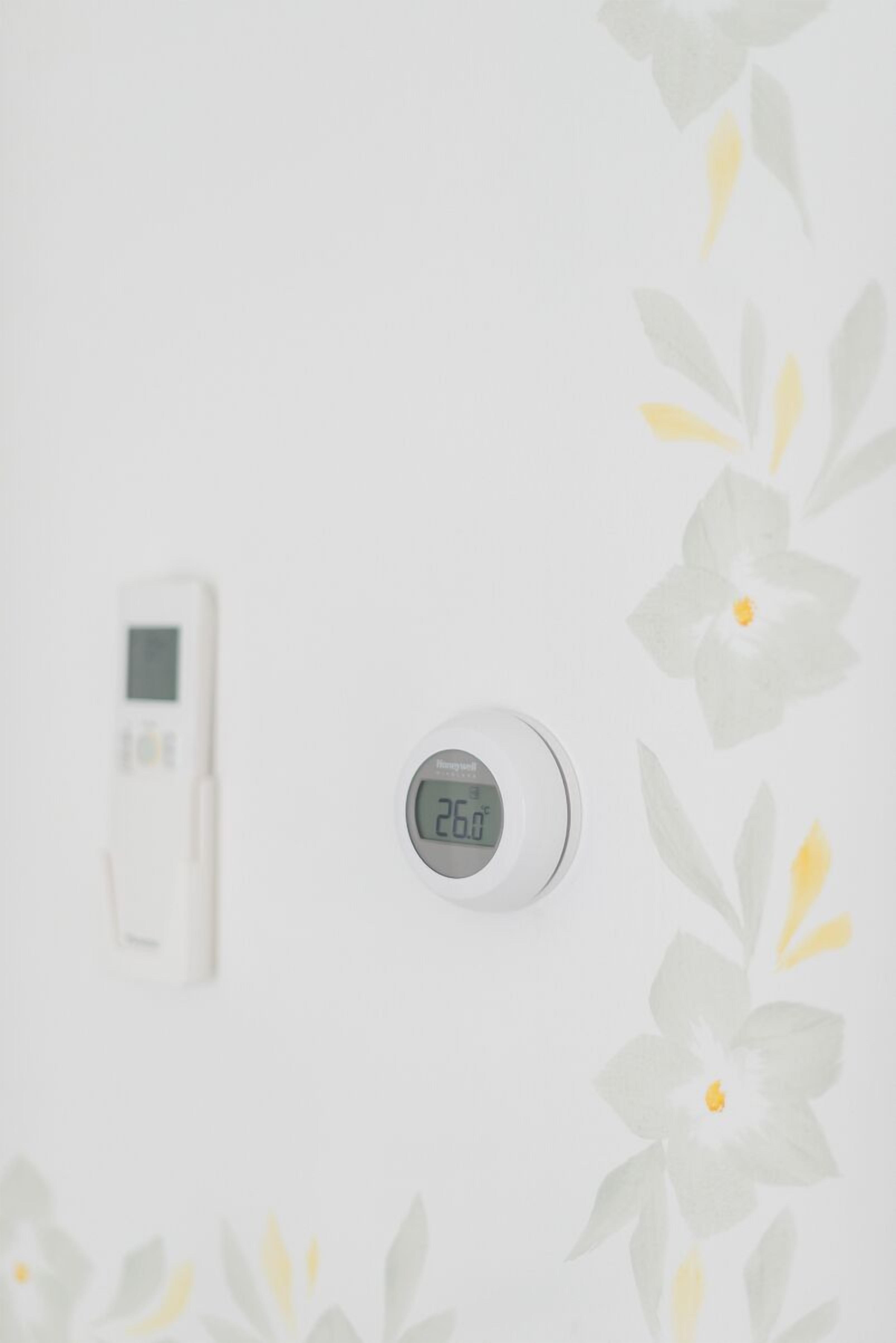 A thermostat and a digital clock on a wall with a floral pattern.