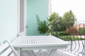 A white outdoor table on a balcony with a metal railing, a light blue wall, and a door in the background. -  Gruppo Luxe Domus (Vigevano)