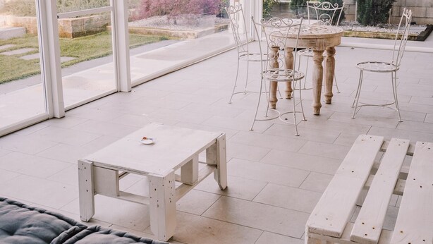 A covered patio with a round table and chairs, a white bench, and a cushioned sofa. -  Gruppo Luxe Domus (Vigevano)