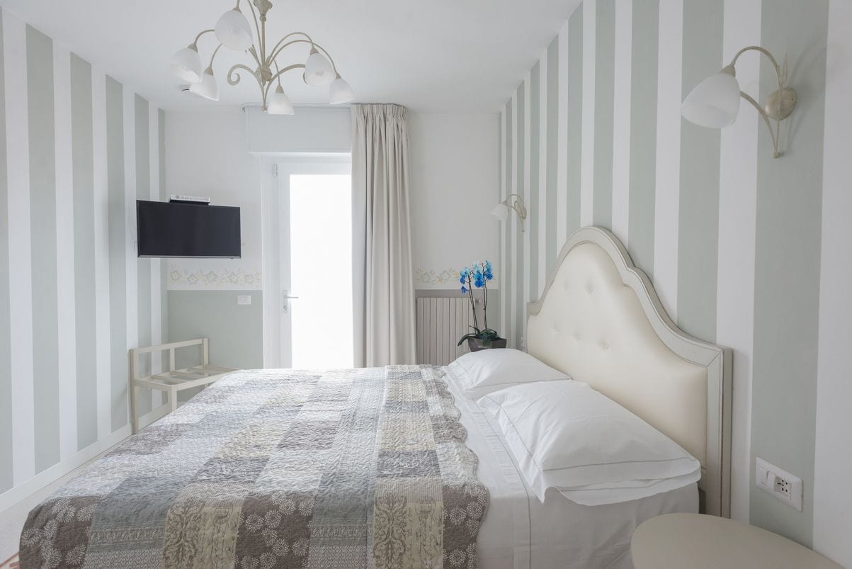 Un dormitorio con una cama grande, un televisor montado en la pared y una mesita de noche con lámpara.