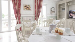 A dining area with white furniture, a clock, and a table set with a cake and teacups. -  Gruppo Luxe Domus (Vigevano)