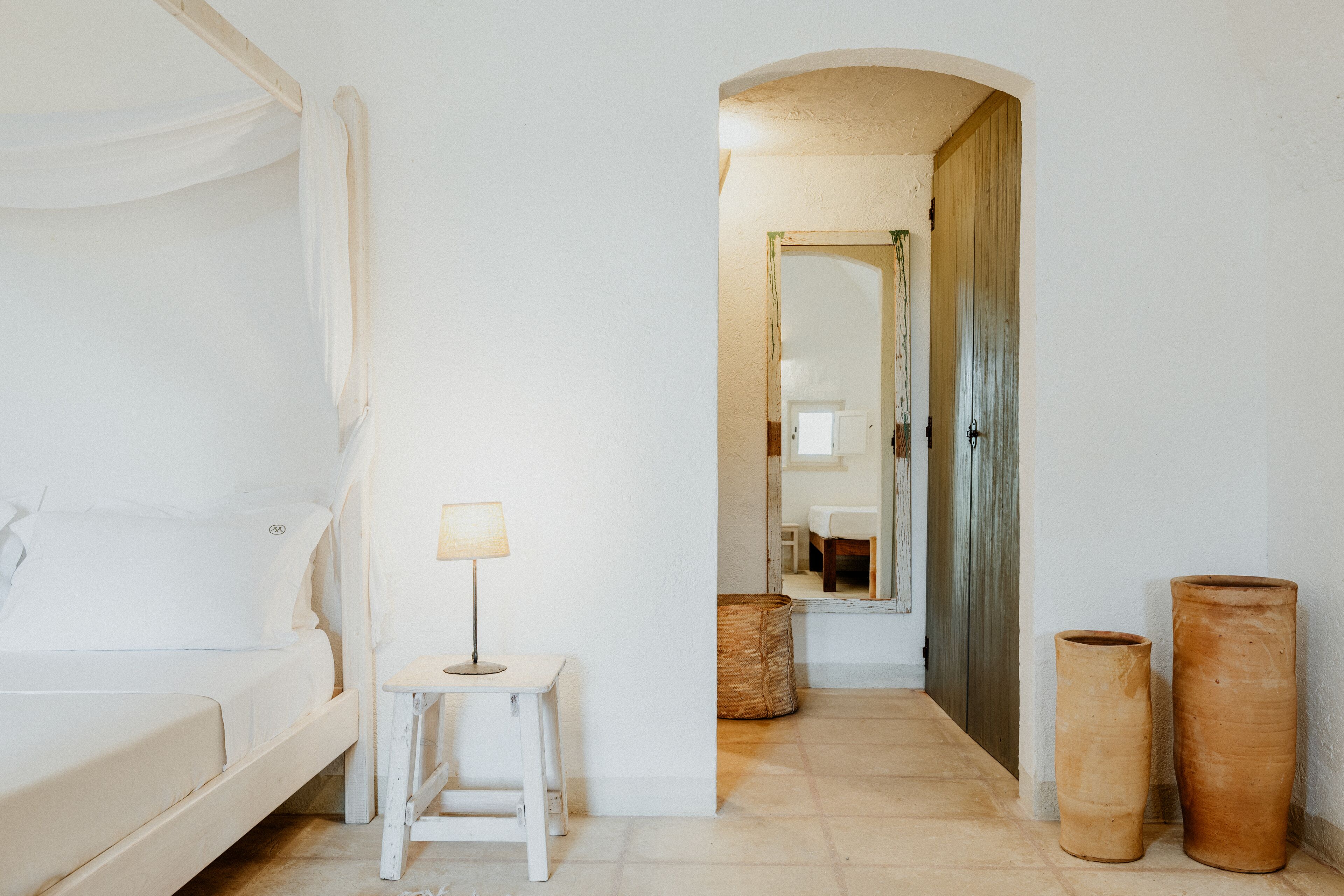 A bedroom with a bed, a bedside table with a lamp, and two large vases.