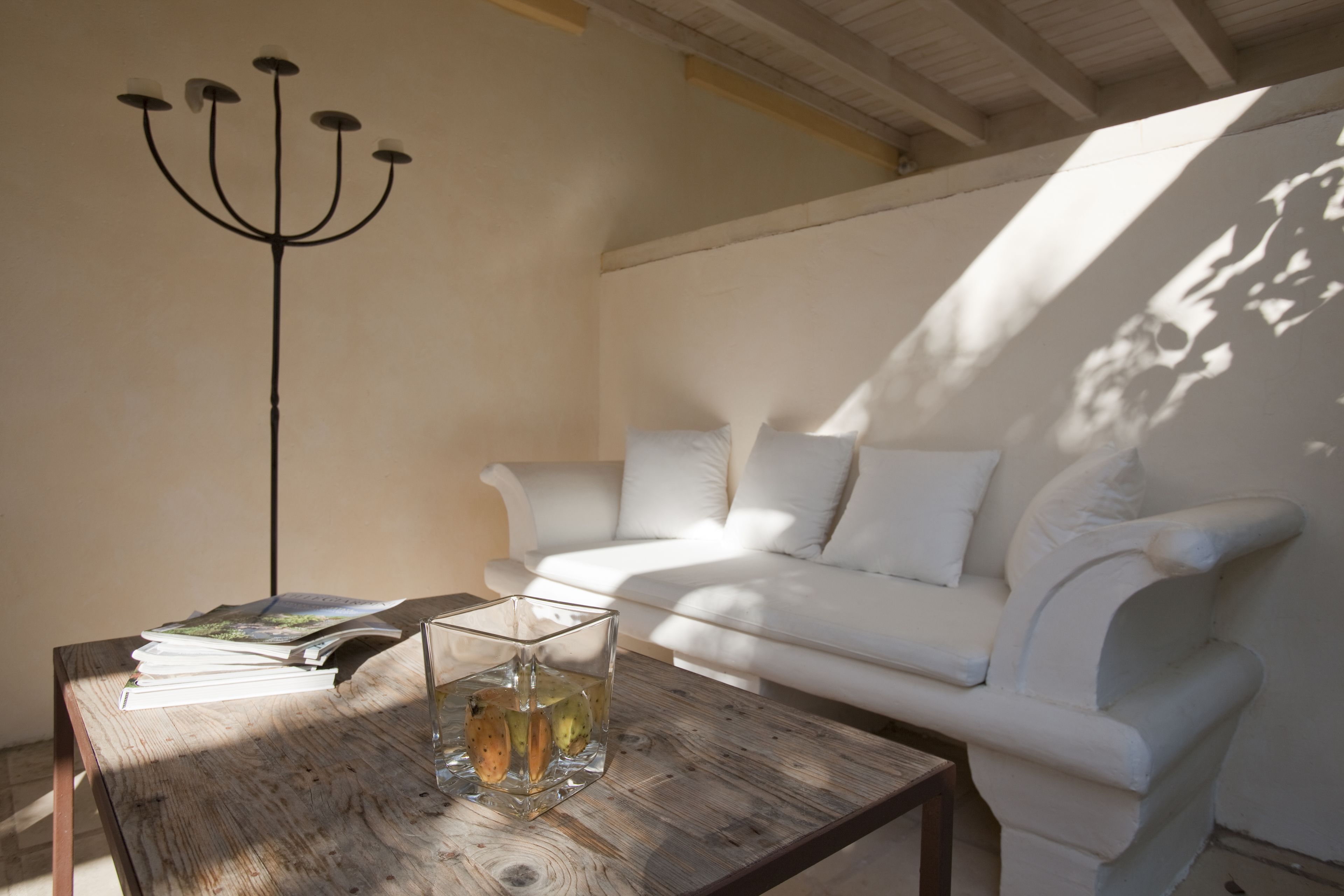 Una habitación con un sofá blanco, una mesa de centro de madera con un jarrón de cristal y libros, y una lámpara de pie negra.