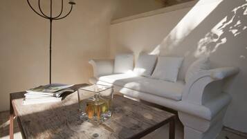 Una habitación con un sofá blanco, una mesa de centro de madera con un jarrón de cristal y libros, y una lámpara de pie negra.