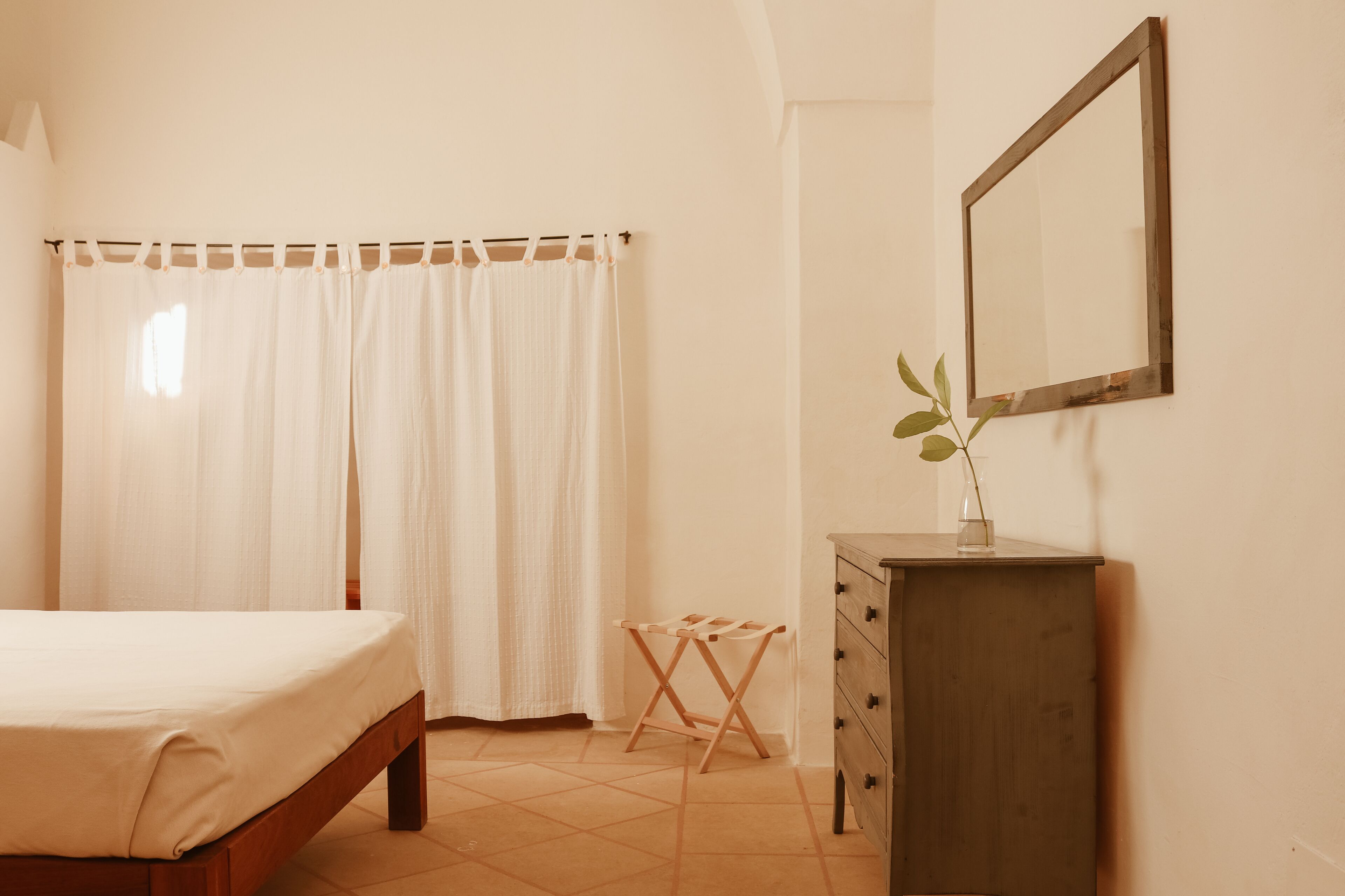 A bedroom with a bed, a dresser, a mirror, and a window with curtains.