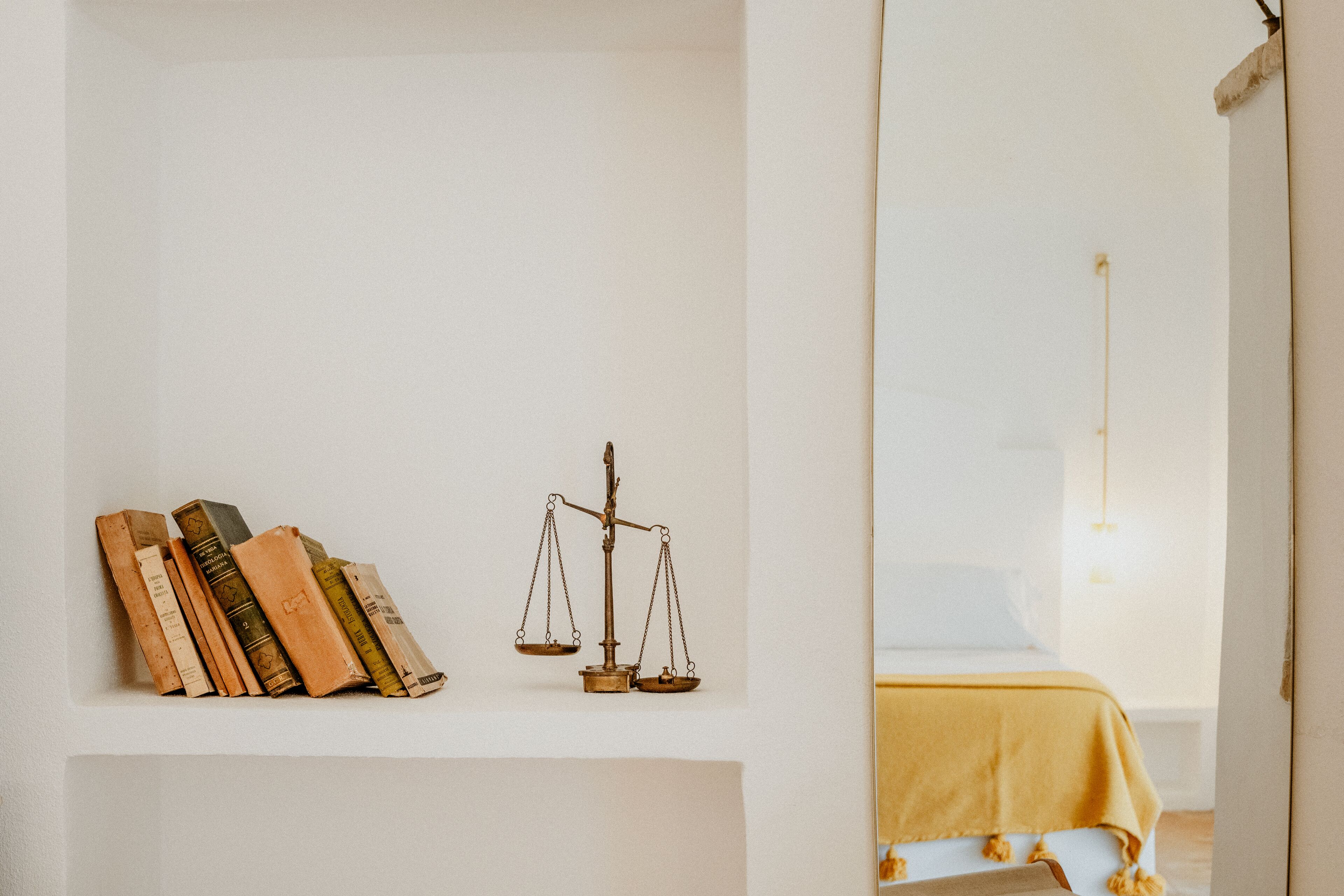 A room with a bed covered in a yellow blanket, a shelf with books and a scale.