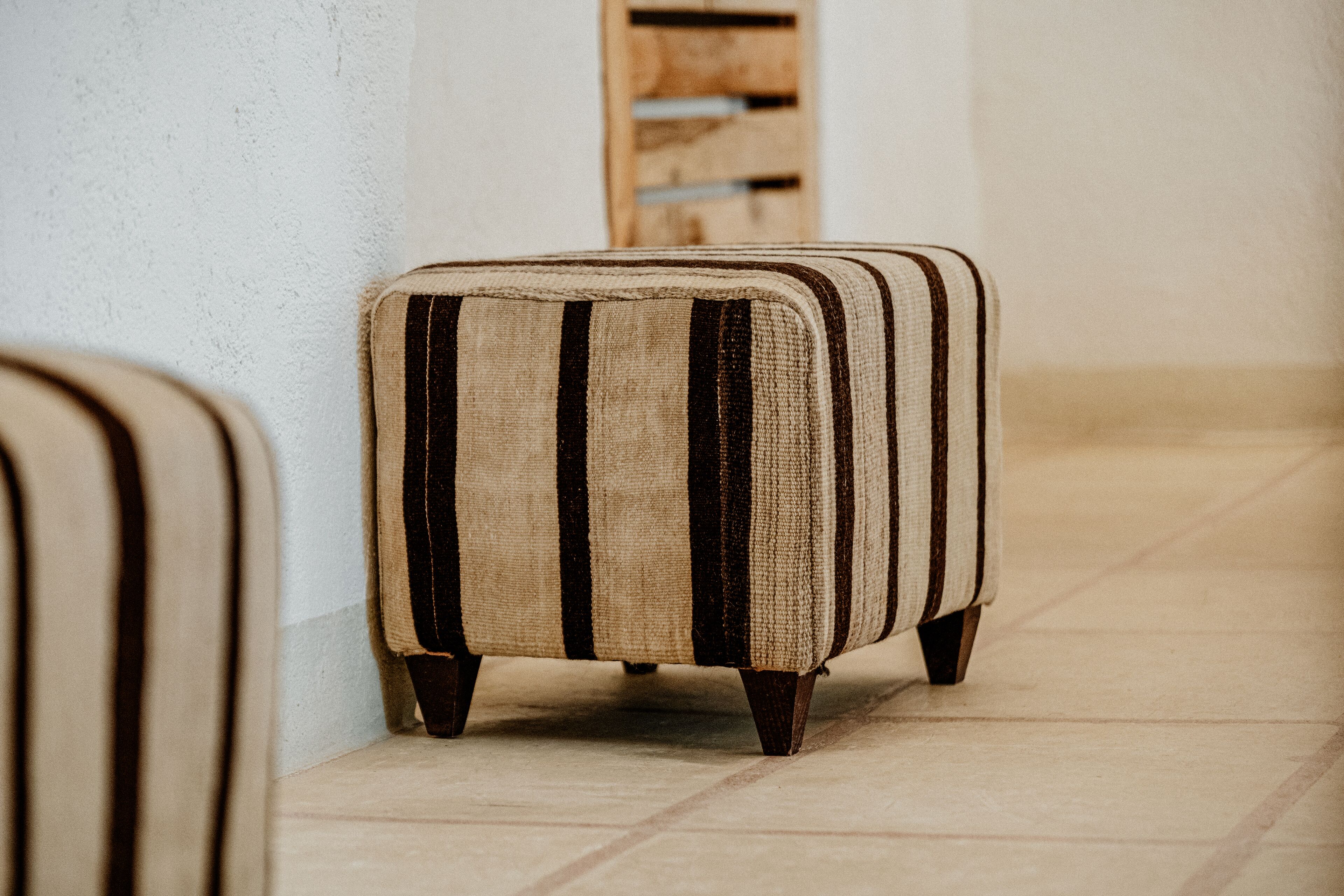 Un pouf rayé dans un couloir, avec un mur lambrissé et un sol carrelé.