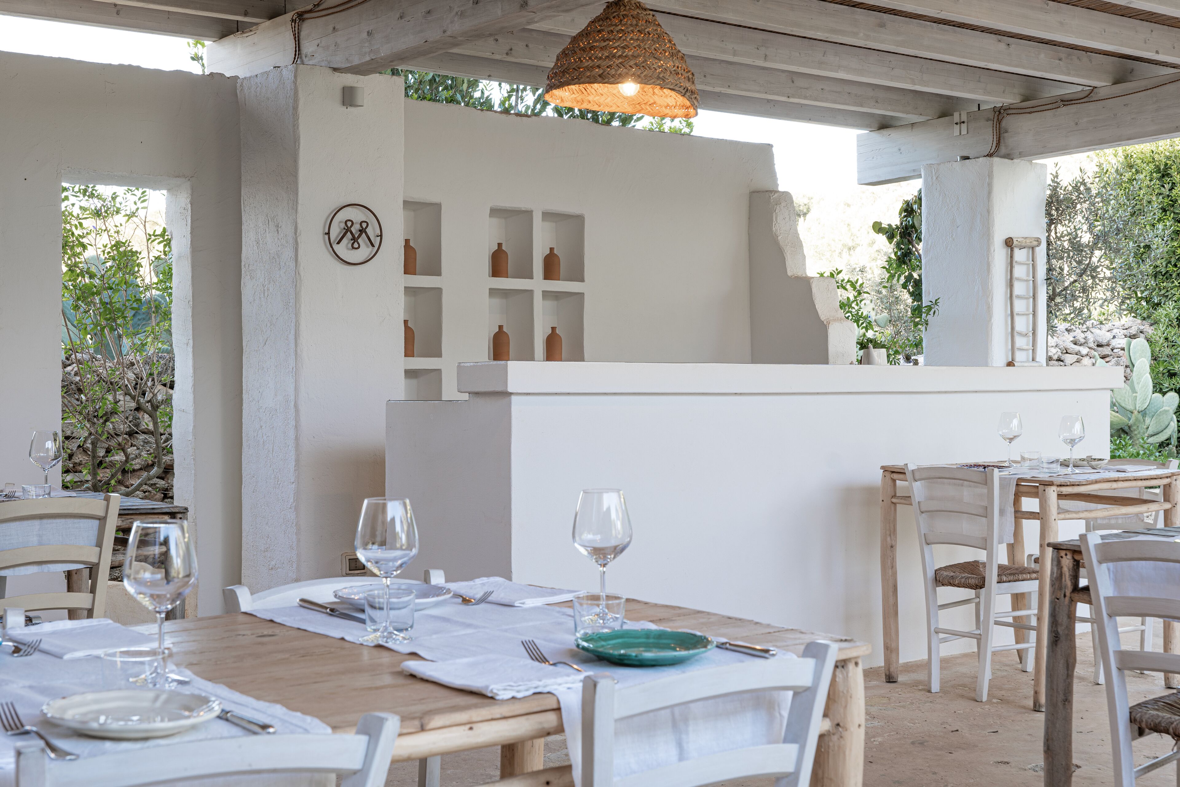A dining area with wooden tables and chairs, white walls, and a central white counter with shelves.