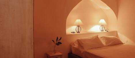 Un dormitorio con una cama, una mesita de noche con lámpara y una planta.