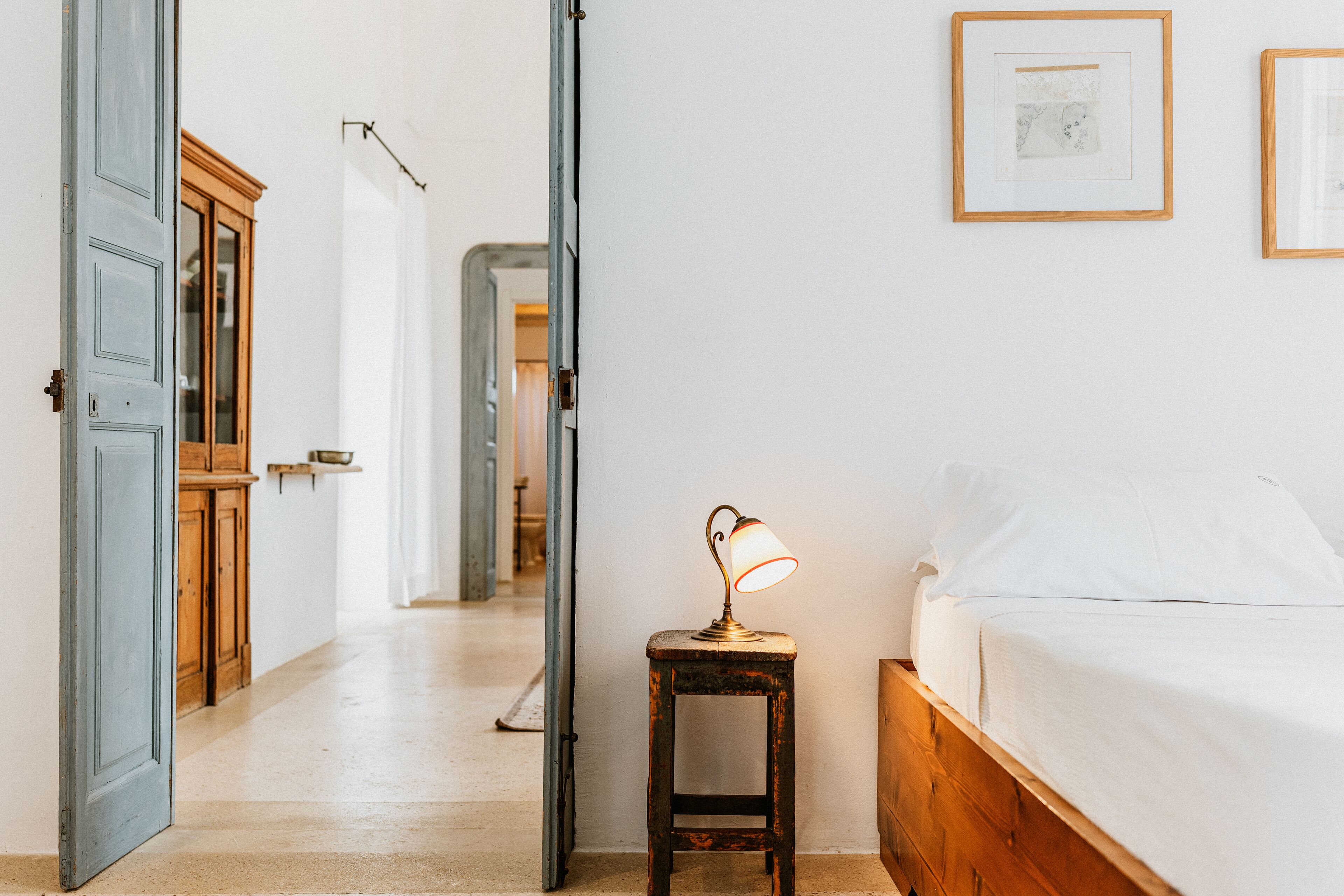 Un dormitorio con una cama de madera, una mesita de noche con lámpara y una puerta que da a otra habitación.