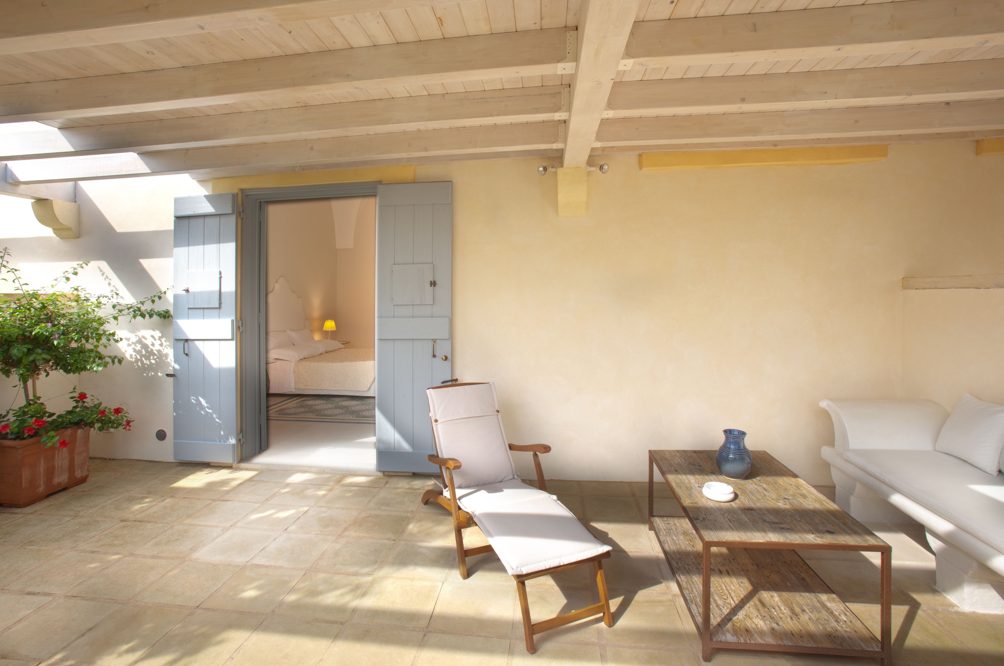 A sunlit room with a wooden ceiling, a white sofa, a wooden table, and a potted plant.