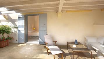 A sunlit room with a wooden ceiling, a white sofa, a wooden table, and a potted plant.