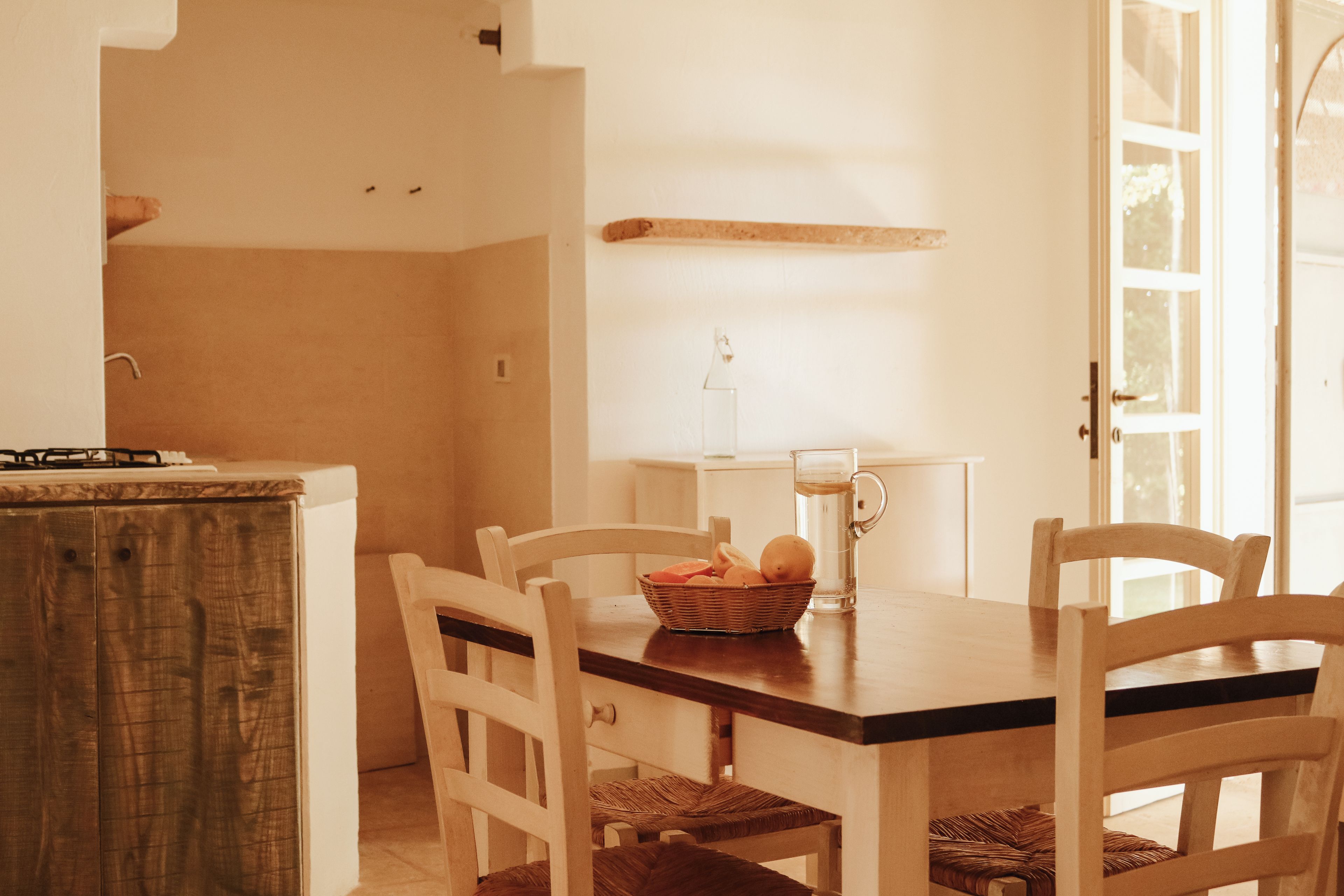 Un comedor con una mesa de madera, sillas blancas y una cesta de fruta.