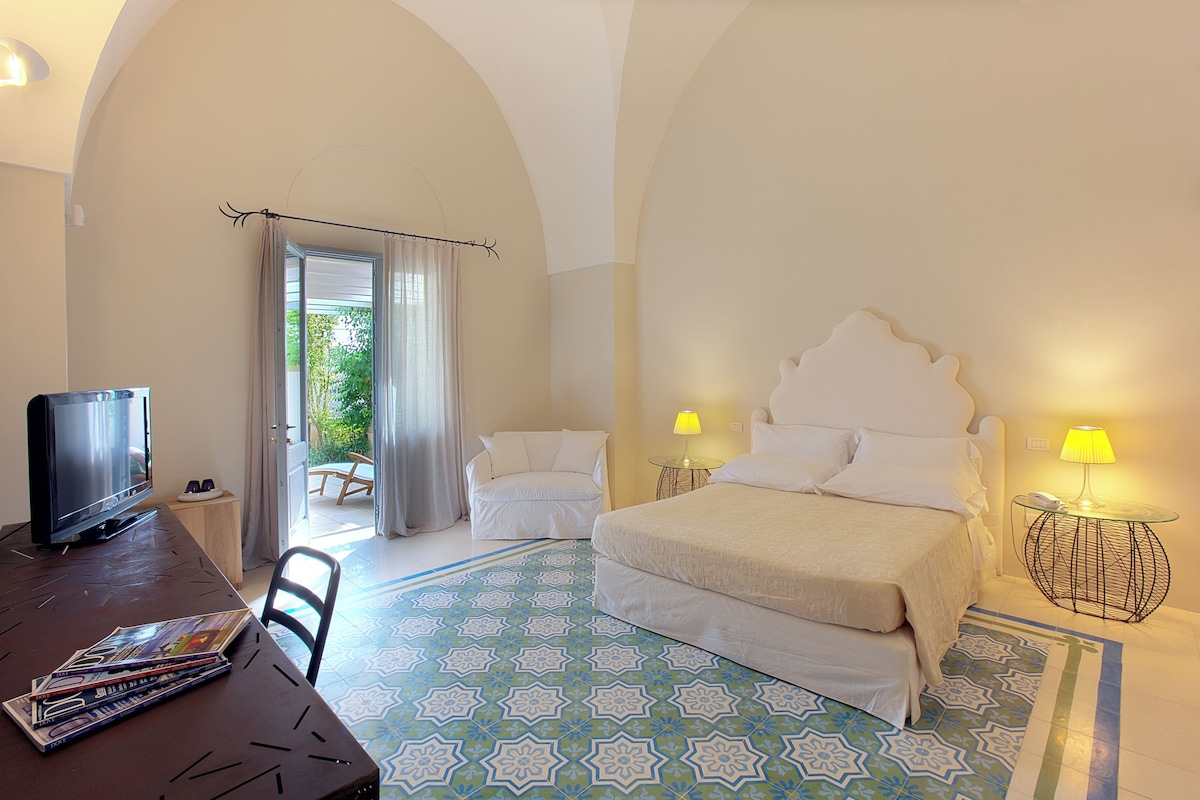 Une chambre d’hôtel avec un grand lit, une télévision, une petite table et une chaise. Elle dispose d’un balcon avec vue sur la verdure.