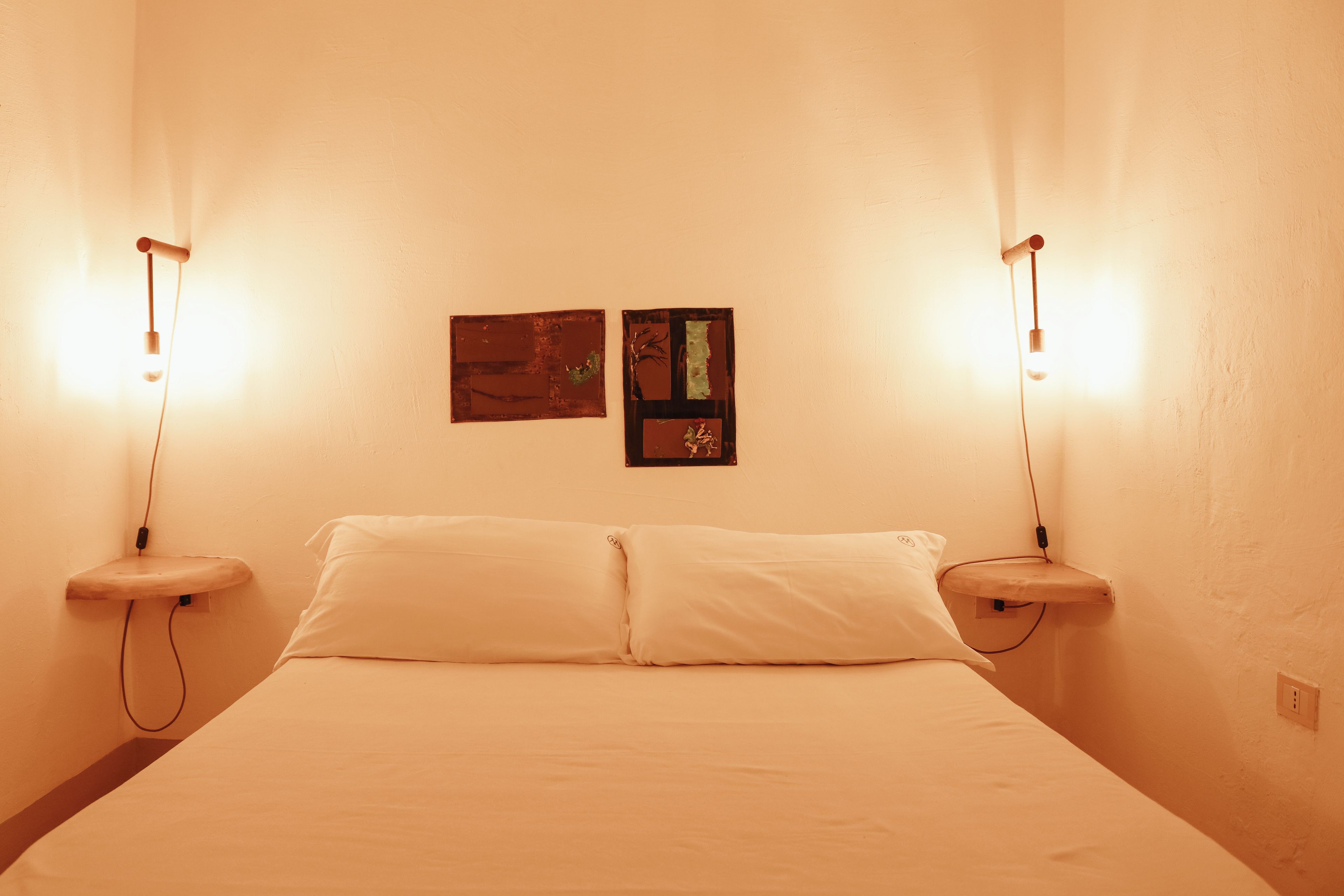 A room with a bed, two wall-mounted light fixtures, and two framed pictures on the wall.