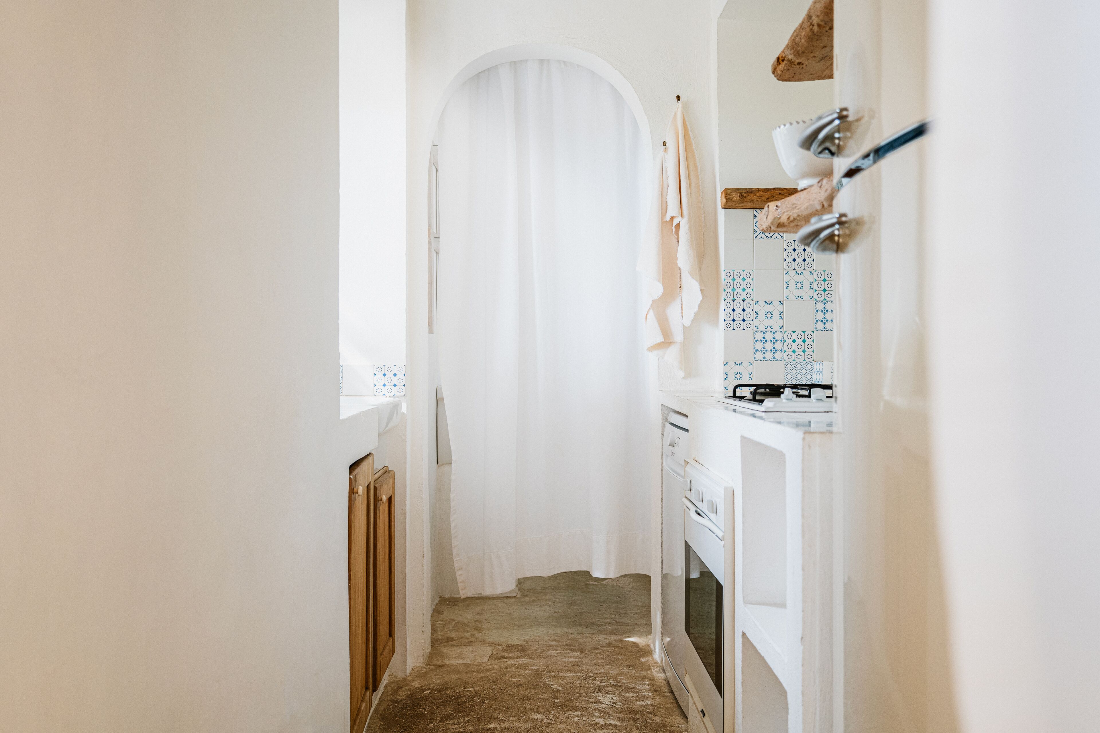 Un pasillo estrecho con una puerta blanca, un salpicadero de azulejos y una estufa blanca.