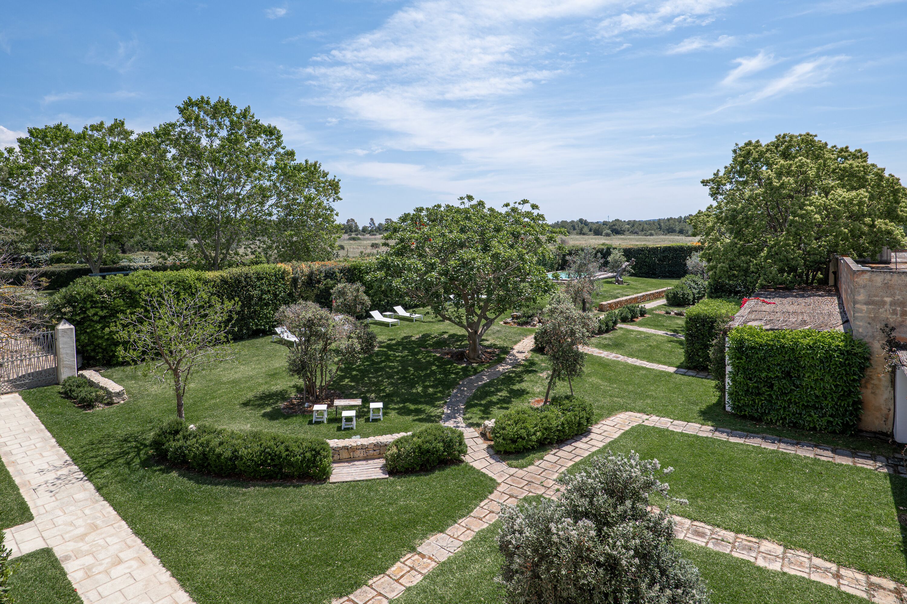 A well-maintained garden with a paved pathway, neatly trimmed hedges, and a variety of trees.