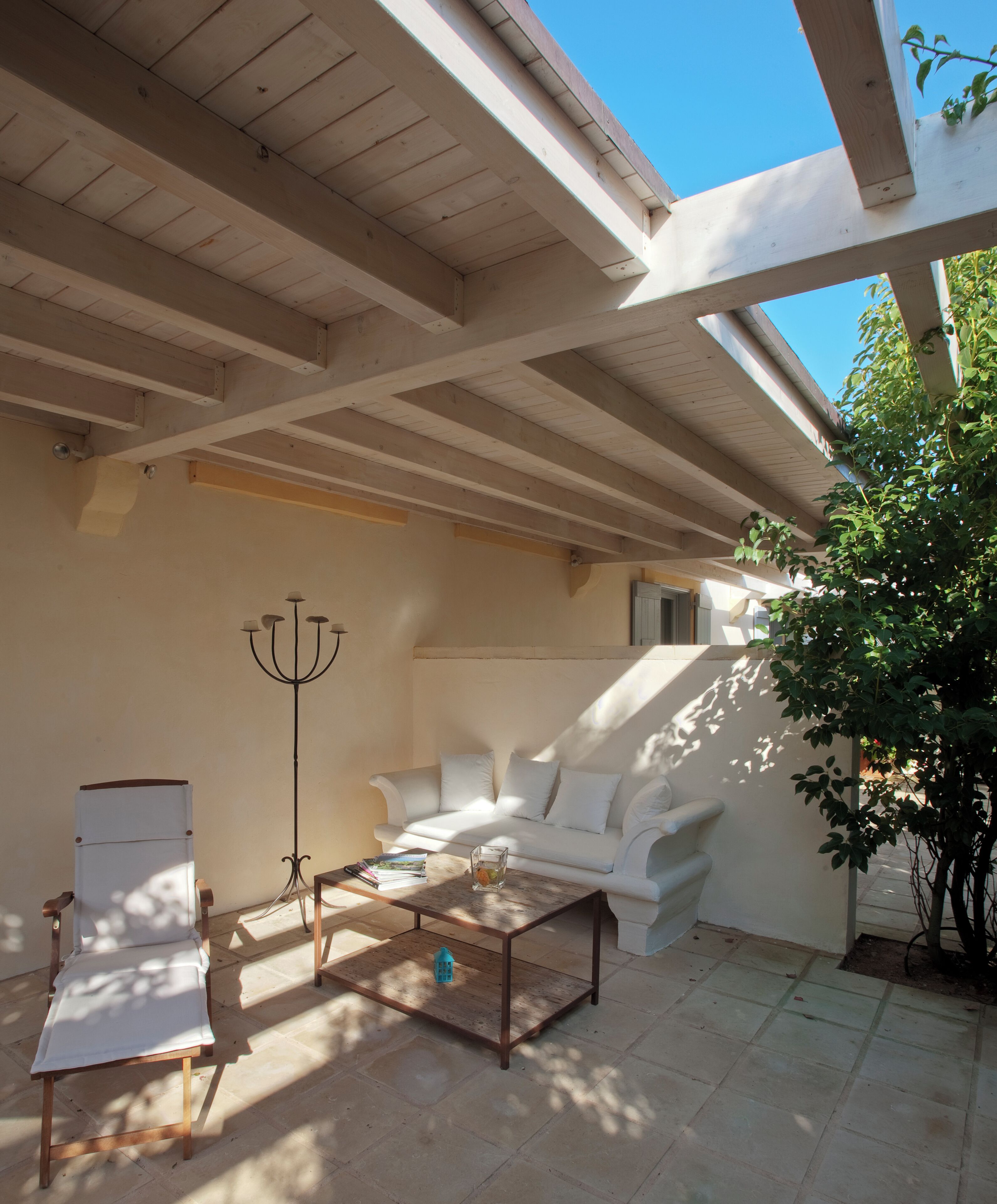 Un patio techado con un sofá blanco, una silla de madera, una mesa de centro y una lámpara de pie.
