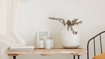 A rustic wooden table with a potted plant, a book, and two bottles, positioned next to a metal chair with a cushion.