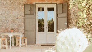 A stone wall, a white door with glass panels, a small table with stools, and a cactus in the foreground. - Masseria Li Foggi (Gallipoli)