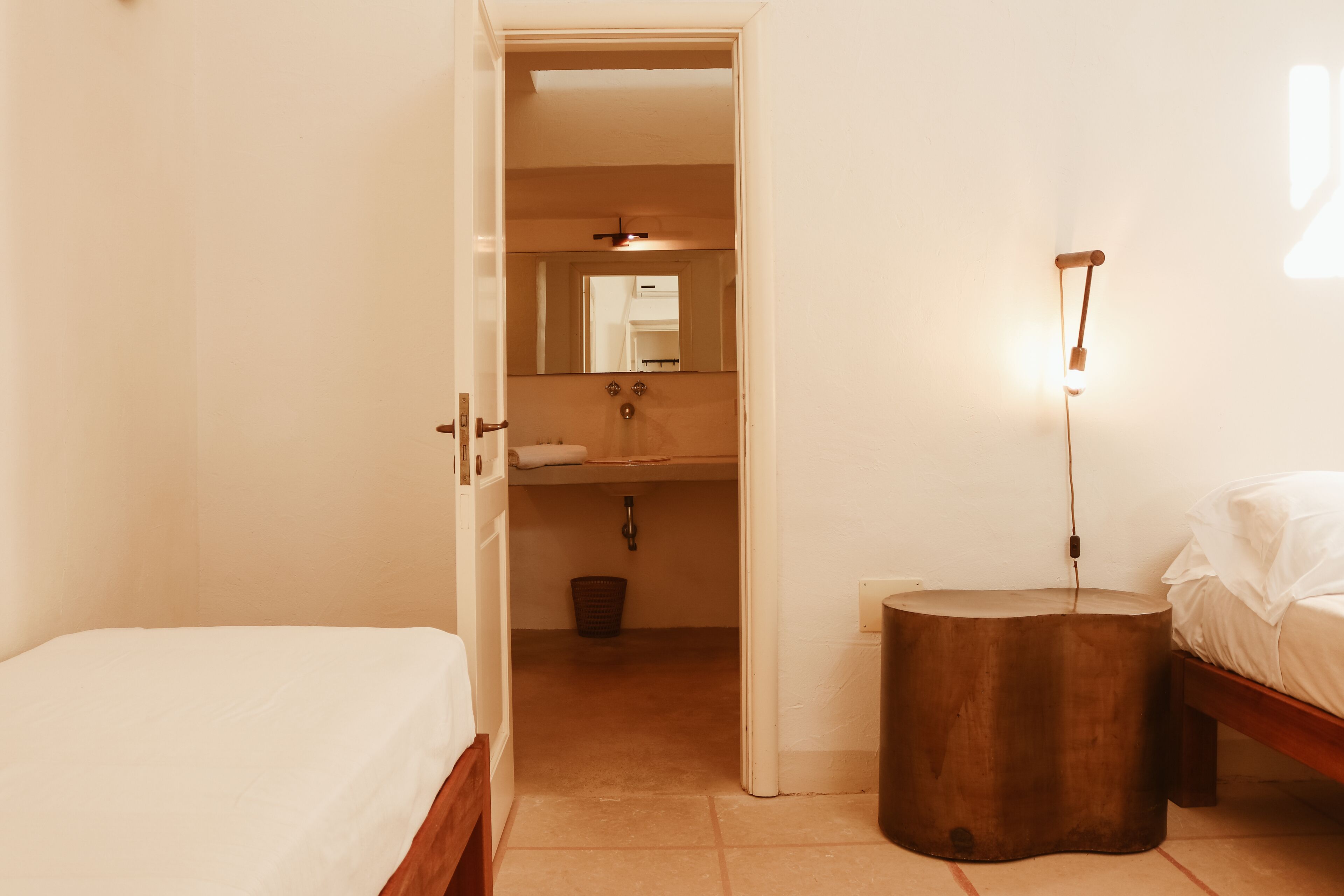 A bedroom with a bed, a round wooden side table, a nightstand, and a mirror on the wall.