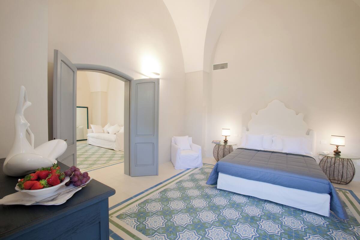A bedroom with a bed, a dresser, a chair, and a table with fruit.