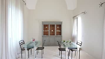 A dining area with a glass table and chairs, a cabinet with dishes, and white curtains.