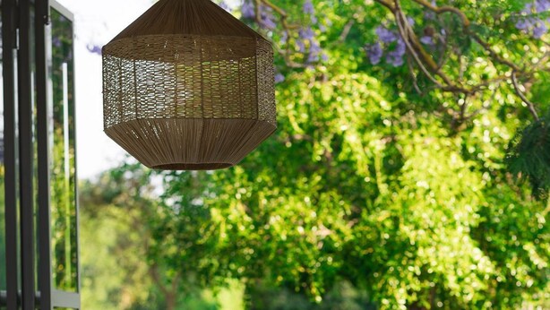 A dining area with tables set for two, a wicker hanging light fixture, and a view of a lush garden. - Masseria Li Foggi (Gallipoli)