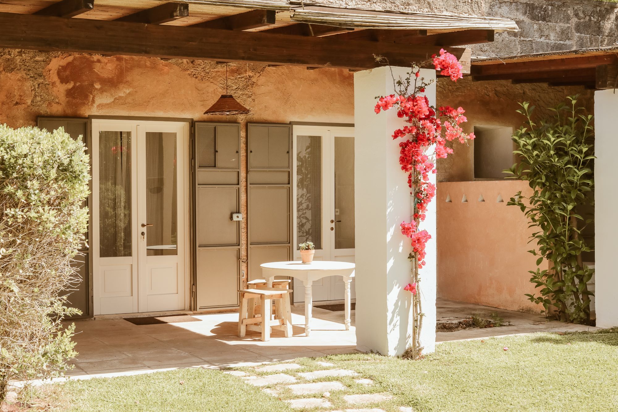 A patio area with a wooden table and chairs, a potted plant, and a flower arrangement.