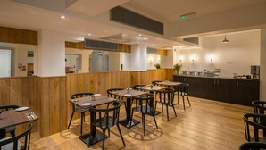 A modern restaurant with wooden paneling, black chairs, and a central island with a kitchen counter. - Pelican London Hotel and Residence (London)