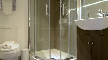Un baño moderno con ducha envuelta en vidrio, inodoro blanco y tocador de madera con lavamanos.