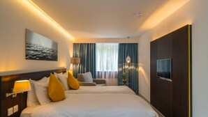 A hotel room with two beds, a TV, a lamp, and a painting on the wall. - Pelican London Hotel and Residence (London)