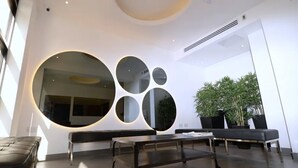 A modern interior with a seating area, a large circular mirror, and potted plants. - Pelican London Hotel and Residence (London)