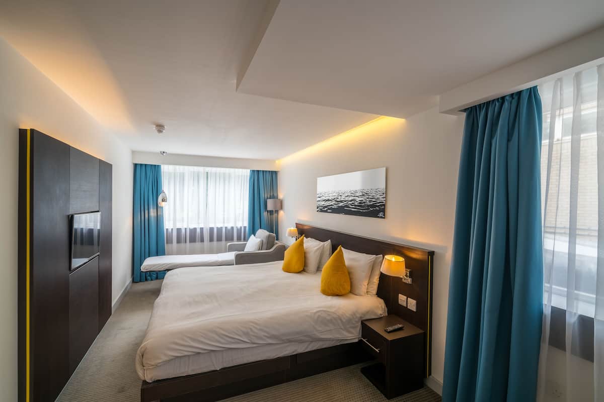 Ett hotellrum med en stor säng, en tv, ett skrivbord och ett fönster med gardiner.