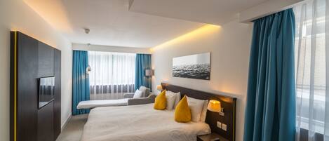 A hotel room with a large bed, a TV, a desk, and a window with curtains.