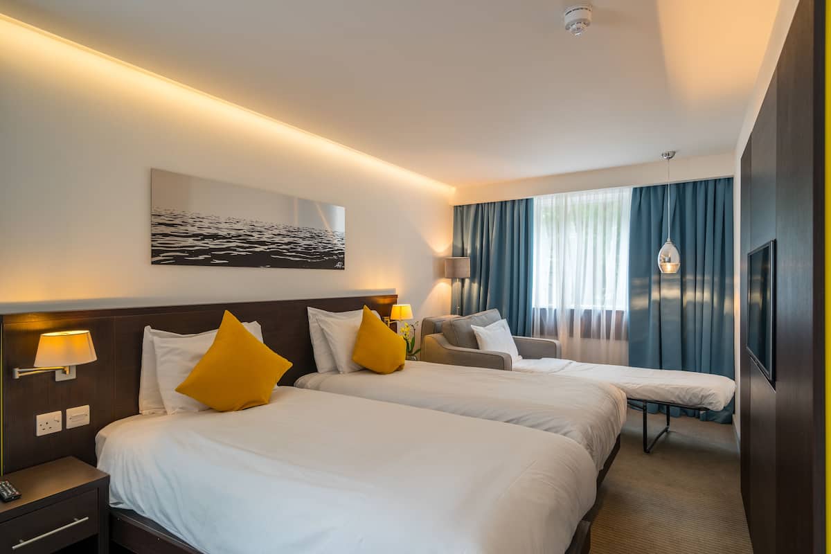 Ett hotellrum med två sängar, ett skrivbord, en stol, en TV och ett fönster med gardiner.