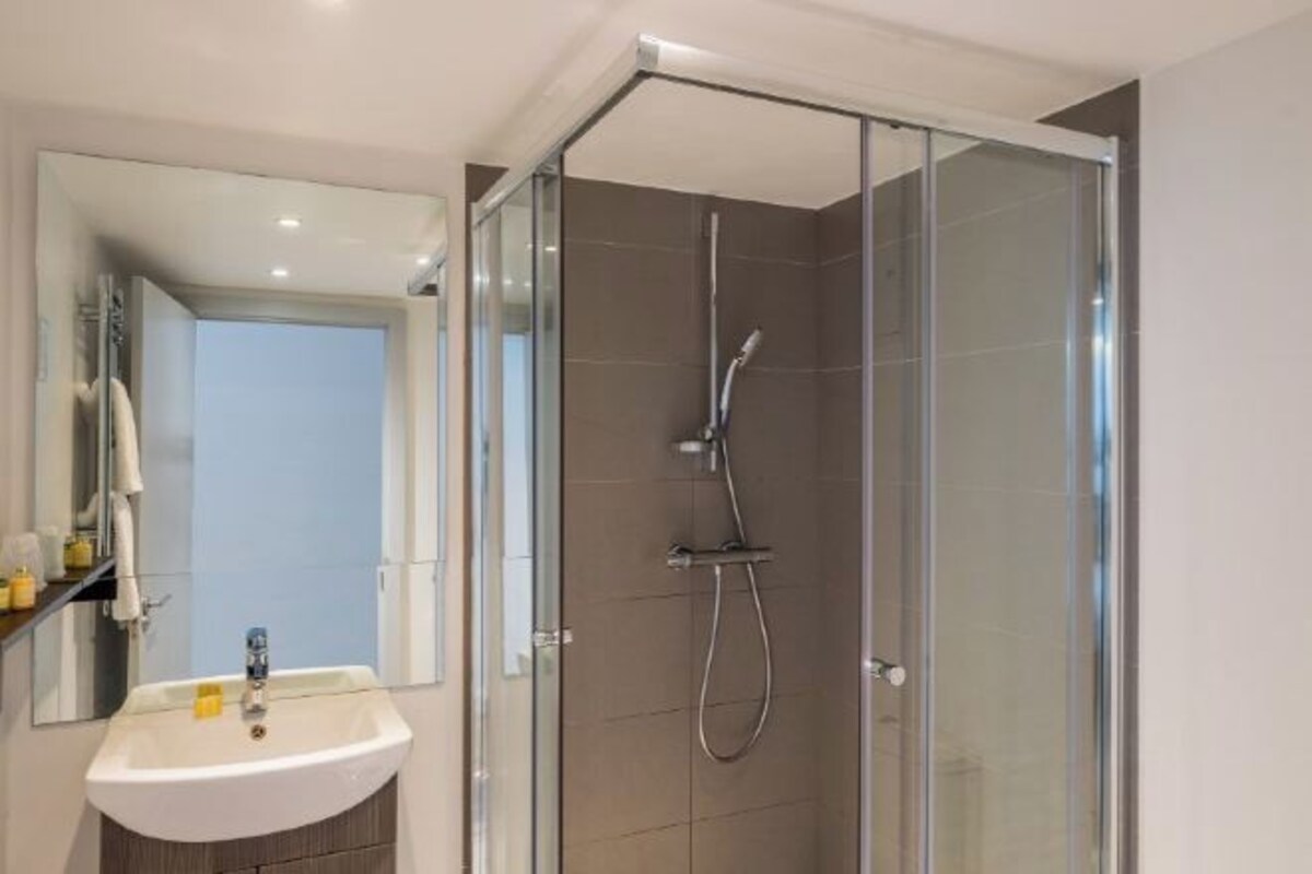 Un baño moderno con cabina de ducha de vidrio, un lavamanos blanco y un espejo.
