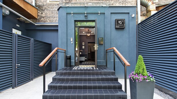 A set of black tiled steps leading to a building entrance with a blue facade, a wooden handrail, and a planter with flowers. - 15th Avenue Hotel (Vilnius)