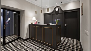 A reception area with a check-in counter, a clock, and a door leading to a hallway. - 15th Avenue Hotel (Vilnius)