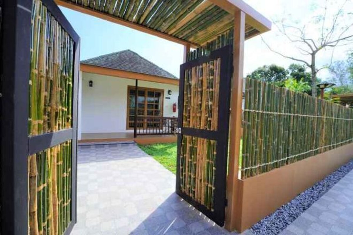 A covered entrance with a bamboo fence, a paved pathway, and a building with a tiled roof.
