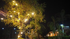 Una escena nocturna de un sendero bordeado de árboles e iluminado con luces de cadena, que conduce a un edificio con un vestíbulo cubierto.