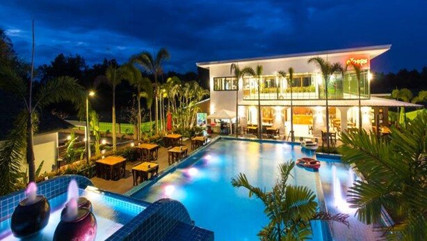 Un hotel moderno con piscina, zona de estar al aire libre y una entrada bien iluminada.