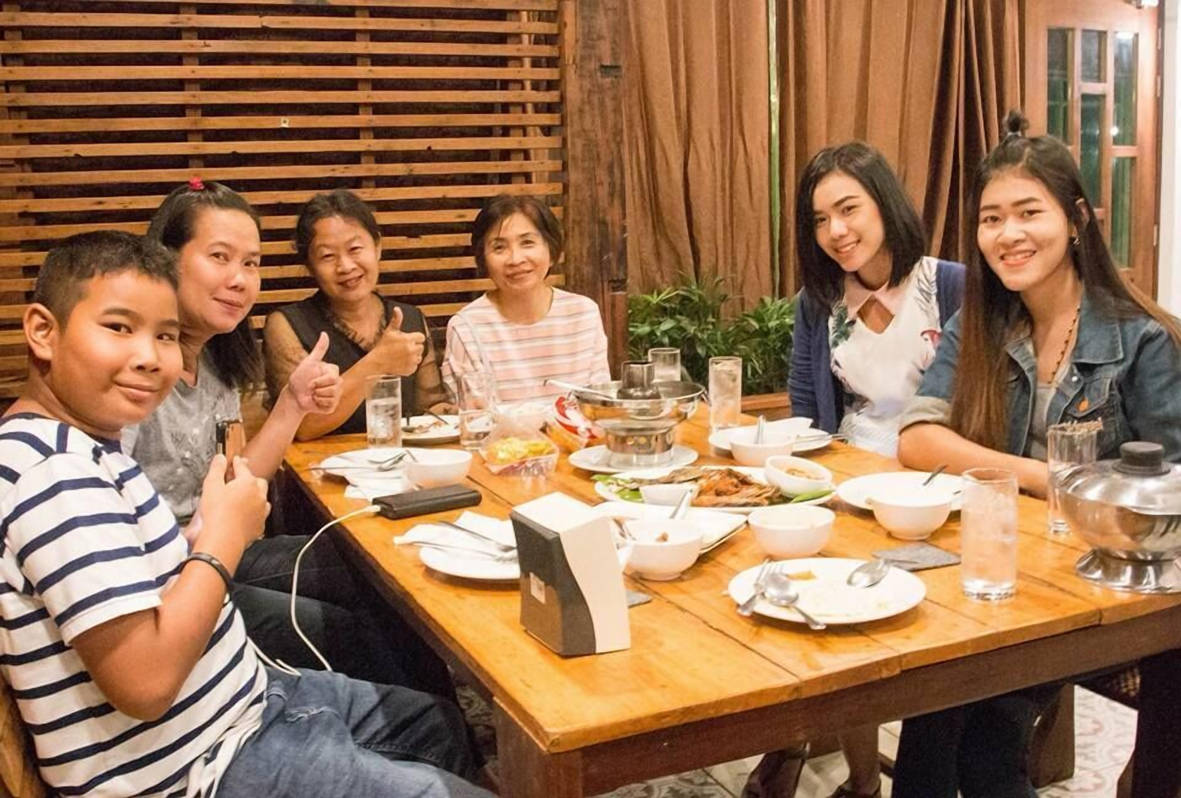 A group of people seated around a wooden table with various dishes and a hot pot.